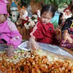 Four-year-old child making kkakdugi (cubed radish kimchi), carefully mixing radish cubes with red pepper seasoning.
