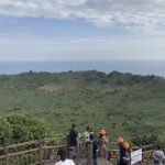 Panoramic view from the summit of 성산일출봉 in Jeju Island, South Korea, overlooking the coastline and surrounding sea.