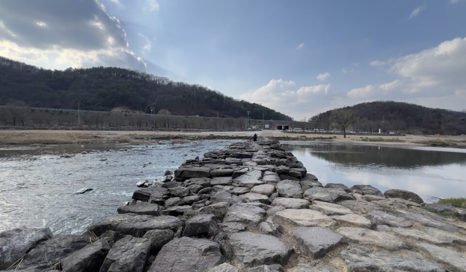 Scenic view of 진천 농다리 from the starting point of the bridge in Jincheon, South Korea, showing the historic stone bridge extending across the river.