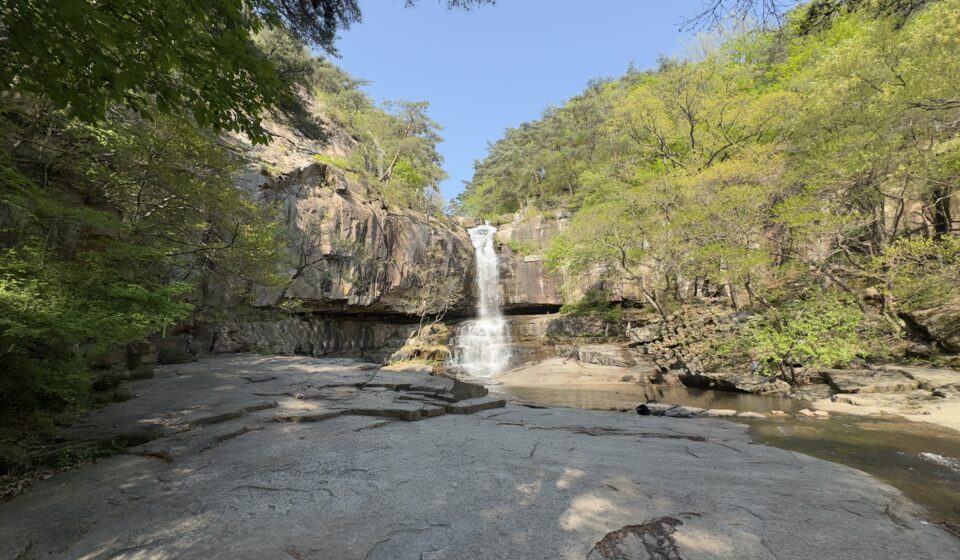 Photo capturing water cascading powerfully at 수옥폭포 in Goesan, South Korea, with clear streams flowing over rocky cliffs.