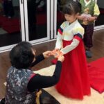 Young girl in traditional hanbok receiving New Year’s money (sebaetdon) from her grandmother after performing a New Year’s bow during Seollal celebration in Korea.