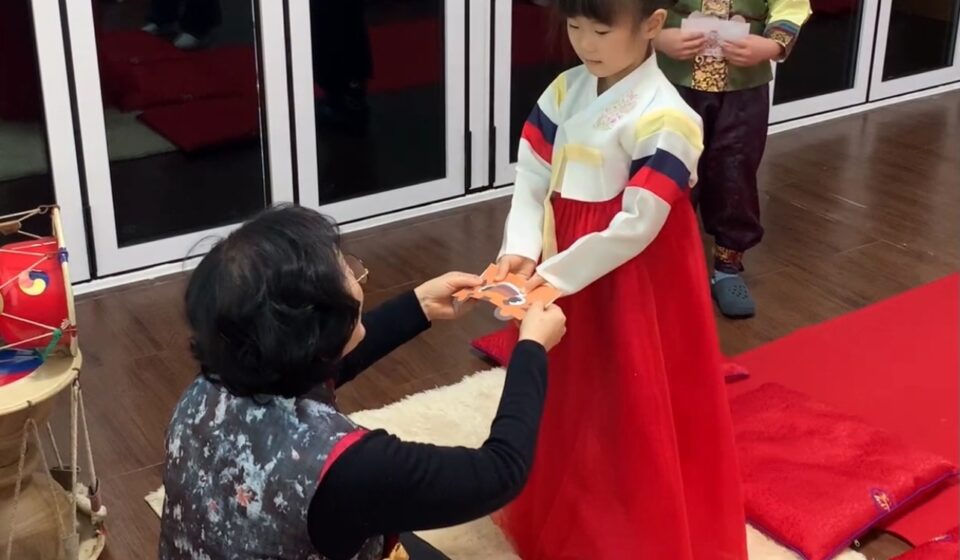 Young girl in traditional hanbok receiving New Year’s money (sebaetdon) from her grandmother after performing a New Year’s bow during Seollal celebration in Korea.