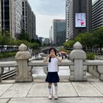 A child standing on a stone bridge overlooking Cheonggyecheon stream with Seoul skyscrapers in the background