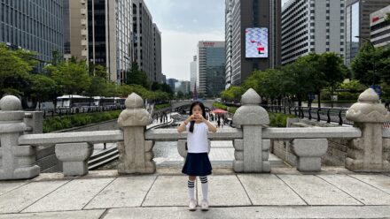 A child standing on a stone bridge overlooking Cheonggyecheon stream with Seoul skyscrapers in the background