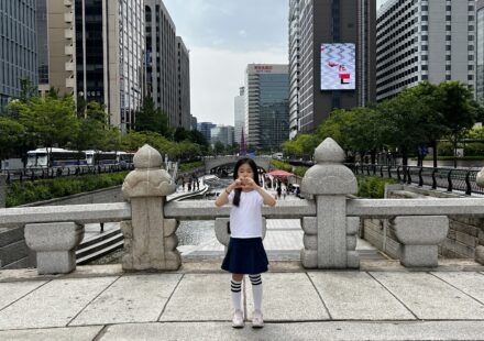 A child standing on a stone bridge overlooking Cheonggyecheon stream with Seoul skyscrapers in the background