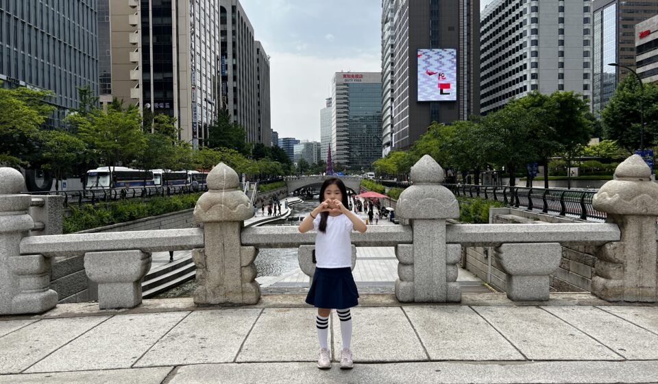 A child standing on a stone bridge overlooking Cheonggyecheon stream with Seoul skyscrapers in the background