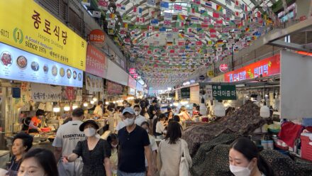 Crowded food alley at Gwangjang Market in Seoul with international flags and traditional Korean street food stalls