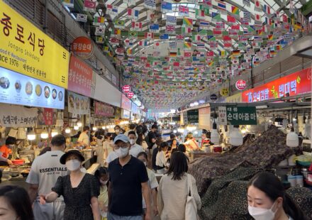 Crowded food alley at Gwangjang Market in Seoul with international flags and traditional Korean street food stalls