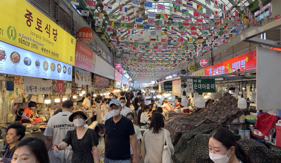 Crowded food alley at Gwangjang Market in Seoul with international flags and traditional Korean street food stalls